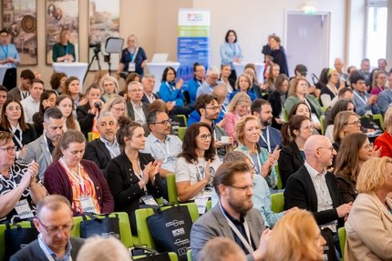 Viele Menschen sitzen in Stuhlreihen in einem großen Raum und klatschen in die Hände