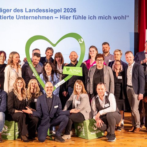 Viele Menschen stehen auf einer Bühne und jubeln, weil sie gerade eine Auszeichnung von der Arbeitsministerin des Landes Sachsen-Anhalt erhalten haben.