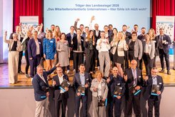 Gruppenfoto der Träger des Landessiegels 2026 „Das mitarbeiterorientierte Unternehmen – Hier fühle ich mich wohl“ aus Sachsen‑Anhalt bei der feierlichen Auszeichnung auf einer Bühne.