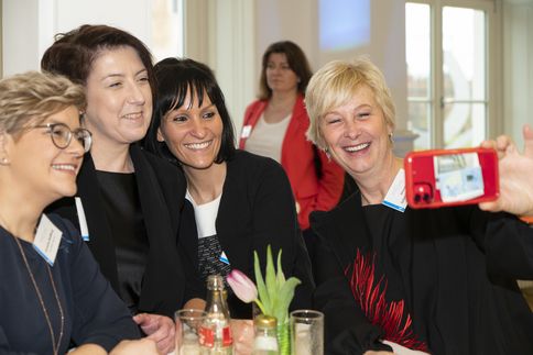 Vier Frauen stehen nebeneinander und lachen in eine Kamera