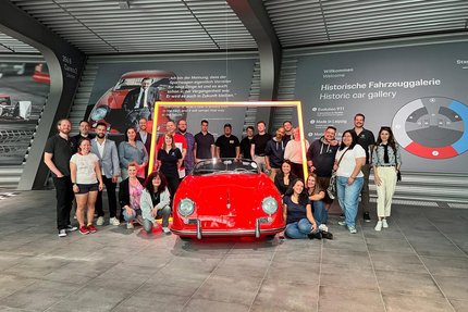 Mitarbeitende von COMAN Software stehen in einer Ausstellungshalle um einen Sportwagen drumherum