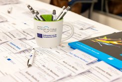 Auf einem Tisch liegen Anmeldelisten, Kugelschreiber und Namensschilder