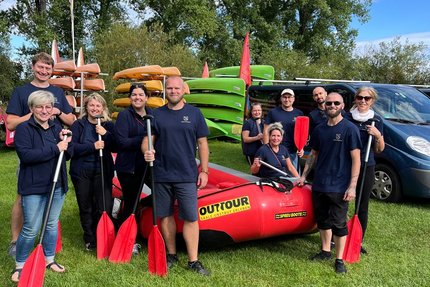 Eine Gruppe Menschen stehen auf einer Wiese vor einem Schlauchboot