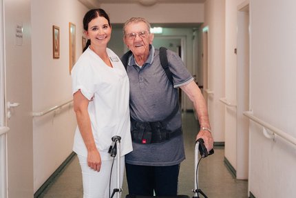 Eine junge Frau und ein alter Mann stehen auf einem Flur in einem Pflegeheim