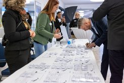 Viele Menschen stehen an einem langen Tisch, auf dem Anmeldelisten, Namensschilder und Kugelschreiber liegen.