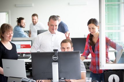 Mehrere Personen aus dem Team der hummelt und partner | Werbeagentur GmbH stehen vor einem Bildschirm. 