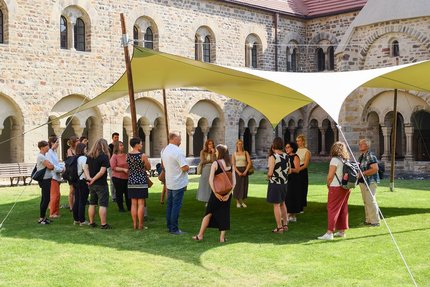eine Gruppe Menschen stehen in einem Innenhof auf der einer Wiese unter einem Pavillon