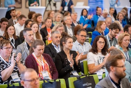 Viele Menschen sitzen in Stuhlreihen in einem Raum und klatschen