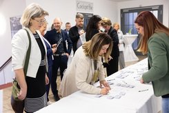 Viele Menschen stehen an einem Registrierungstisch, tragen sich in Listen ein und nehmen ihr Namensschild entgegen.