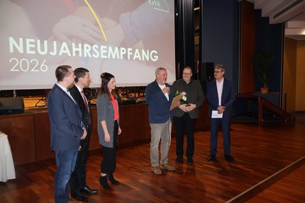 Eine Gruppe Menschen stehen auf einer Bühne. Im Hintergrund ist eine große Leinwand.