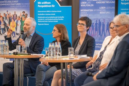 Fünf Menschen sitzen im Halbkreis. Davor stehen zwei Stehtische.