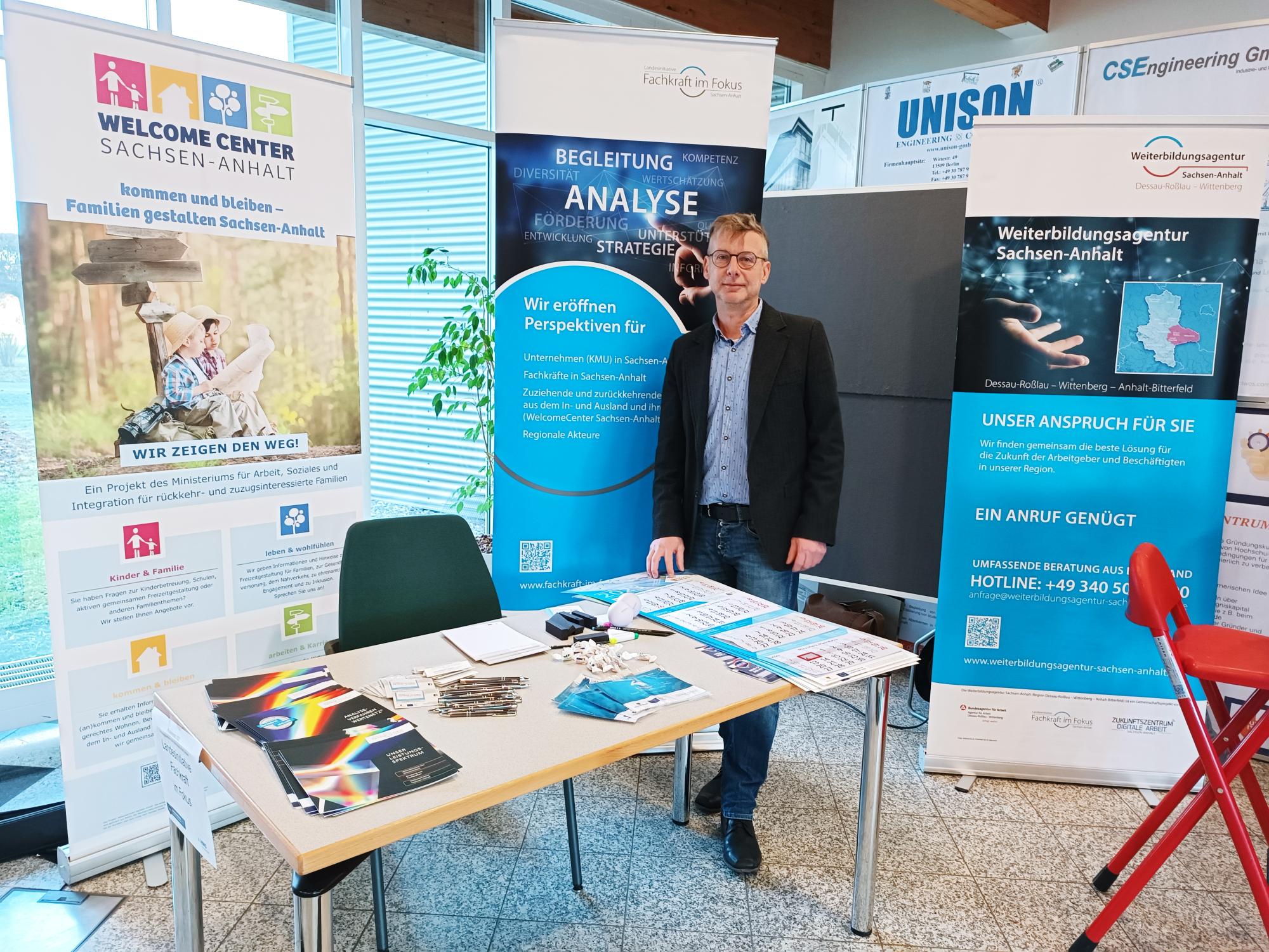 Ingo Faber steht am Messestand von der Landesinitiative Fachkraft im Fokus. Im Hintergrund zahlreiche Roll-ups.