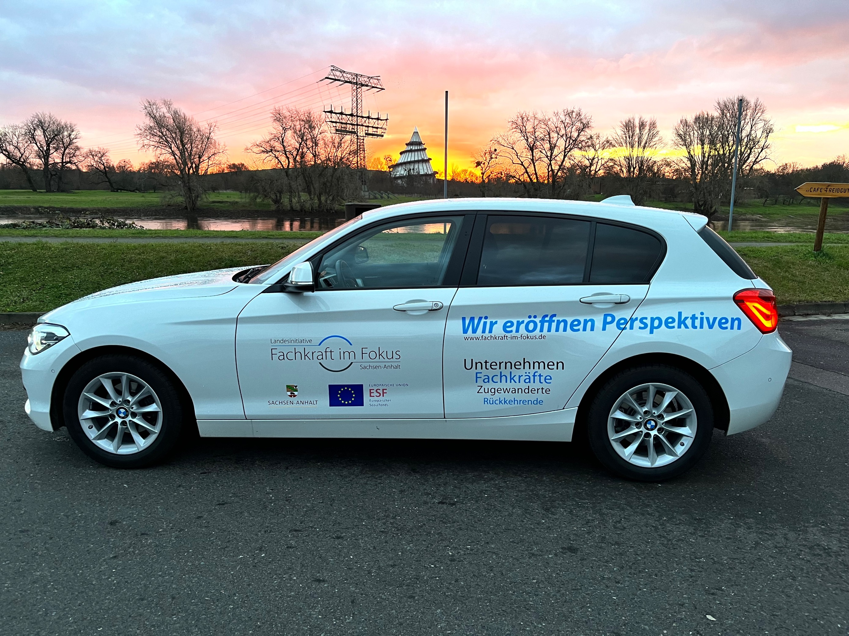 Das Firmenauto von Fachkraft im Fokus steht vor einem schönen Sonnenaufgang im Hintergrund sieht man den Jahrtausendturm aus Magdeburg.